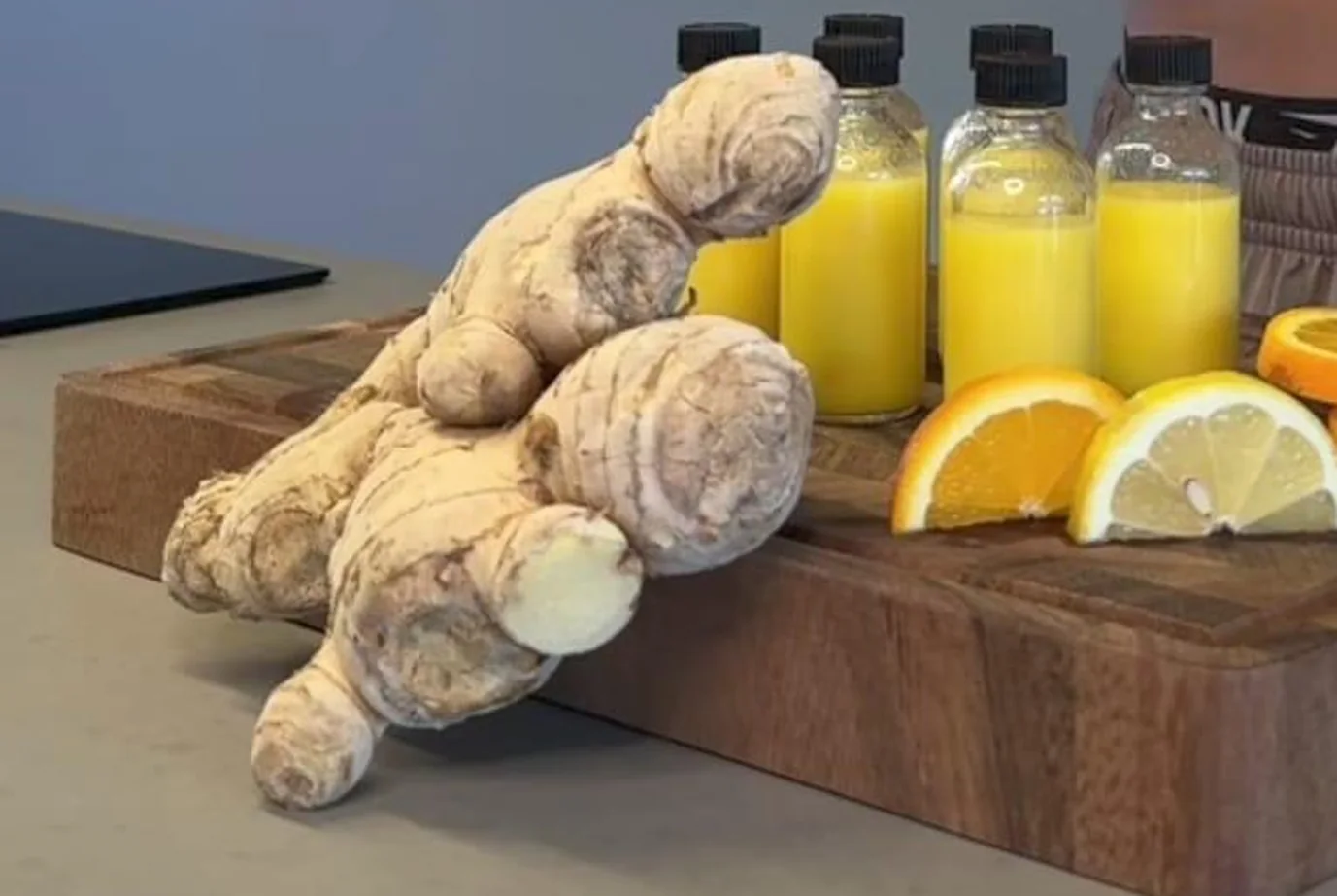 Rhizomes de gingembre frais, tranches d'orange et de citron sur une planche en bois, à côté de flacons de préparation